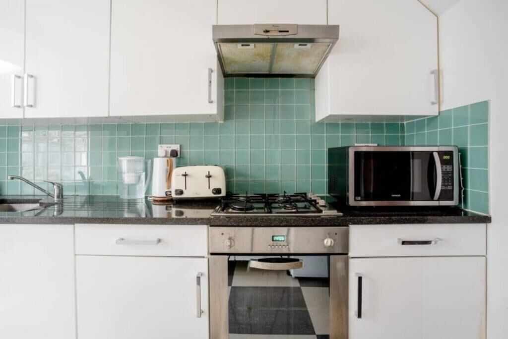 Una cocina con armarios blancos, estufa a gas, microondas y tostadora.
