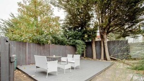 Una terraza con sillas blancas y una mesa, rodeada por una valla de madera y árboles.