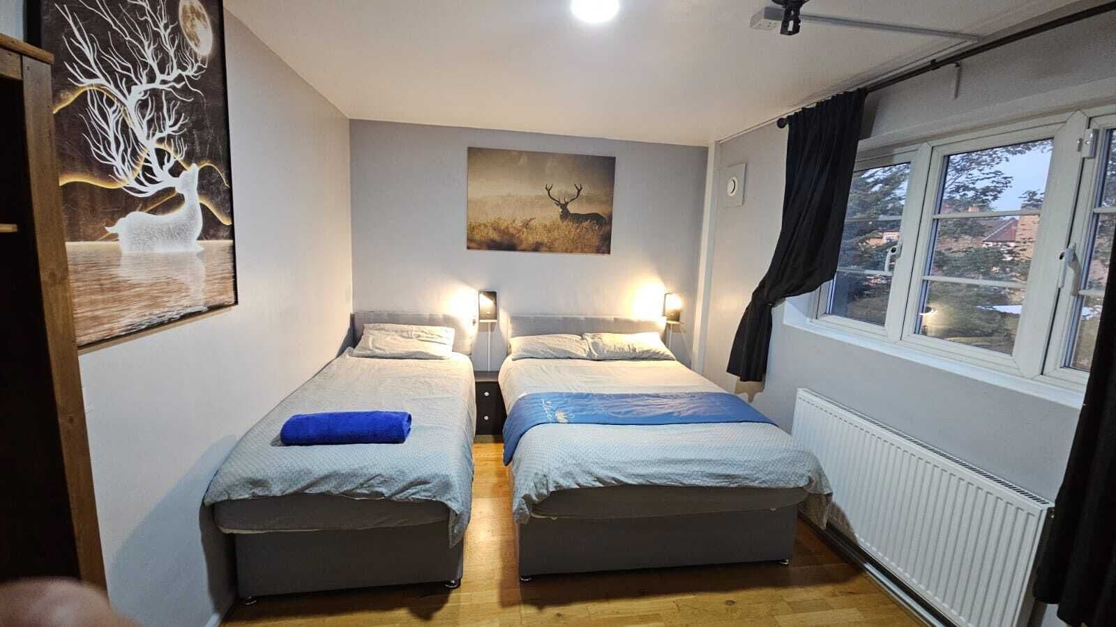 A room with two beds, a nightstand, a wall-mounted painting, and a window with curtains.