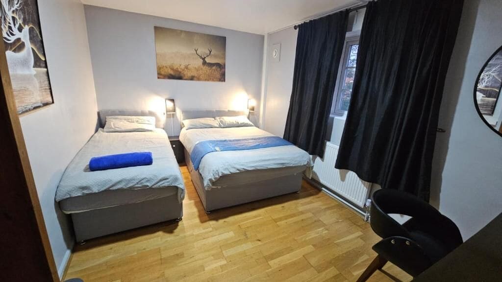 Una habitación con dos camas, una silla, un cuadro y una ventana con cortinas.