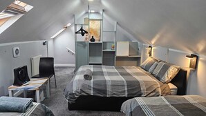 Un dormitorio moderno y compacto con techo estilo loft, cama con ropa de cama a rayas, escritorio con silla y radiador.