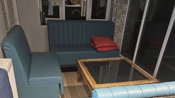 Una habitación con un sofá azul, un cojín rojo y una mesa de centro de cristal.