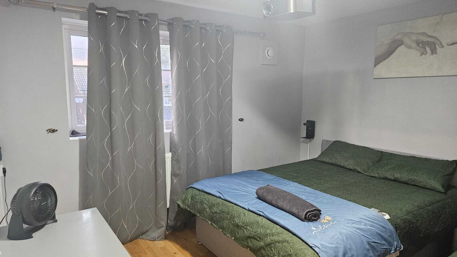 A bedroom with a bed, a desk, and a window with curtains.