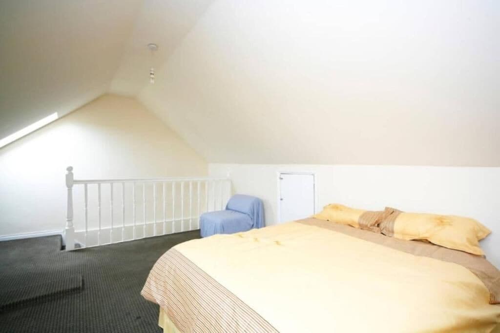 Una habitación con una cama, una silla, una puerta y una barandilla blanca.