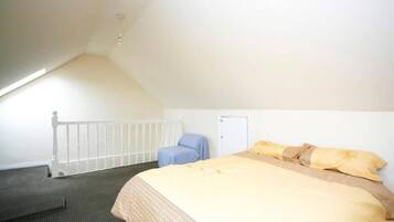 Una habitación con una cama, una silla, una puerta y una barandilla blanca.
