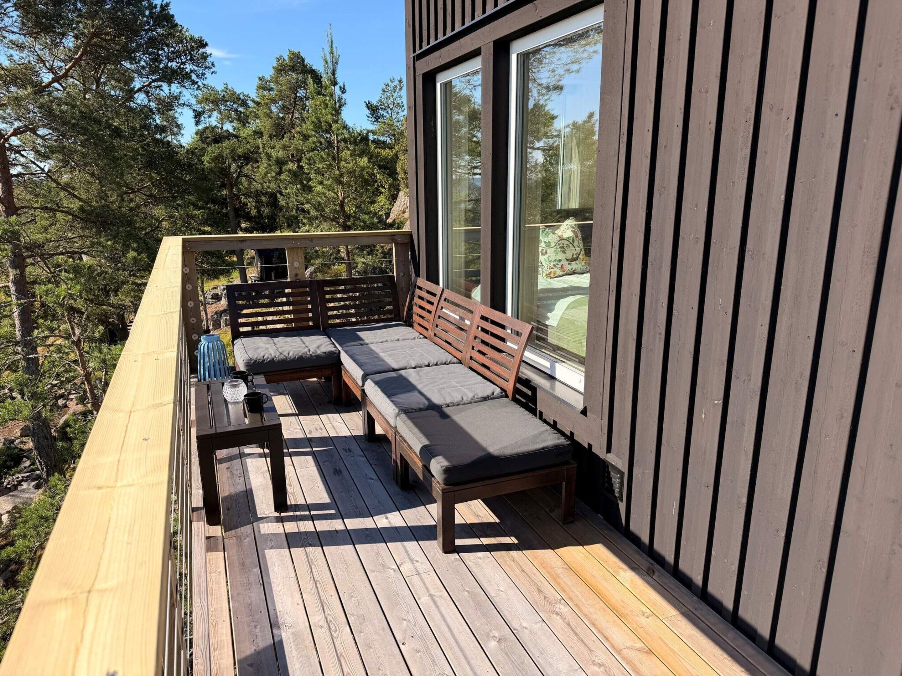 A wooden deck with a built-in bench and a table, overlooking a forested area.