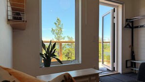 Una habitación con un ventanal grande, una planta en maceta, un banco y una puerta corredera que da a un espacio exterior.