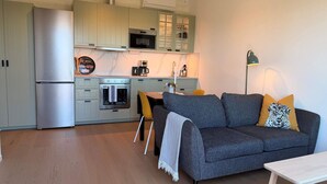 Cocina compacta con refrigerador, horno, microondas y una zona de comedor con sofá y mesa.