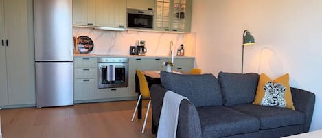 A compact kitchen with a refrigerator, oven, microwave, and a dining area with a sofa and table.