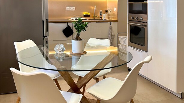 A modern kitchen with a glass dining table, white chairs, a potted plant, and built-in appliances. - Casa Verde | Minimal & Cozy Stay (Elliniko)