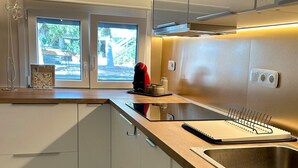 A modern kitchen with white cabinets, a stainless steel sink, a window with a view, and a kettle on the counter. - Casa Verde | Minimal & Cozy Stay (Elliniko)