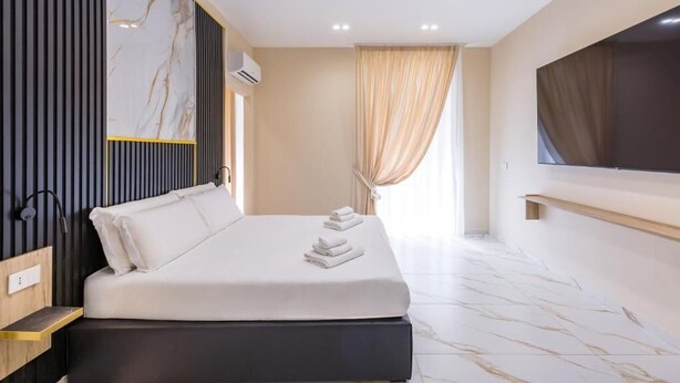 Una habitación de hotel moderna con una cama grande, un televisor de pantalla plana, un muro con diseño de mármol y una ventana con cortinas.