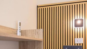 Una habitación moderna con un estante de madera, un dispositivo electrónico negro y una pared con listones verticales y una lámpara.
