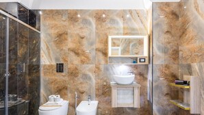 Un baño moderno con paredes de mármol, cabina de ducha de vidrio, un bidé, un inodoro, un lavabo y un espejo.