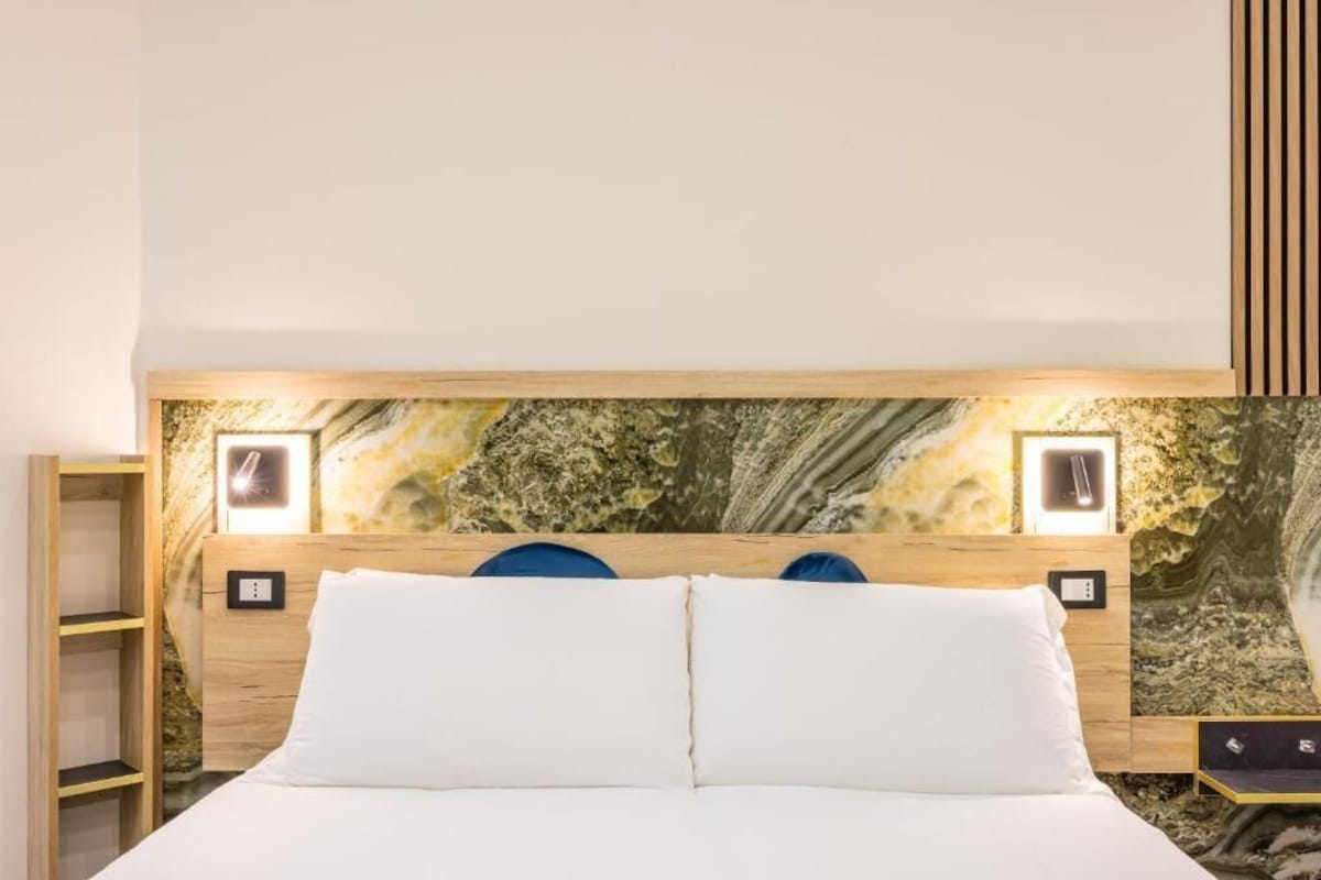 Un letto con biancheria bianca, una testiera in legno e una parete con motivo decorativo.