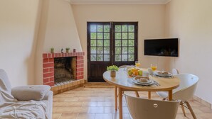 A dining area with a brick fireplace, a table set with plates, glasses, and a TV mounted on the wall. - #394 Albufeira Escape | 3-Bedroom Villa with Shared Pool (Albufeira)