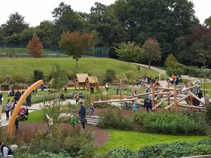Ein Park mit hölzernen Spielgeräten, einem kleinen Holzhaus und einer Rasenfläche.