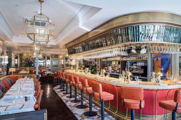 Eine Bar mit einer langen Theke, mehreren Hockern sowie verschiedenen Bartools und Gläsern.