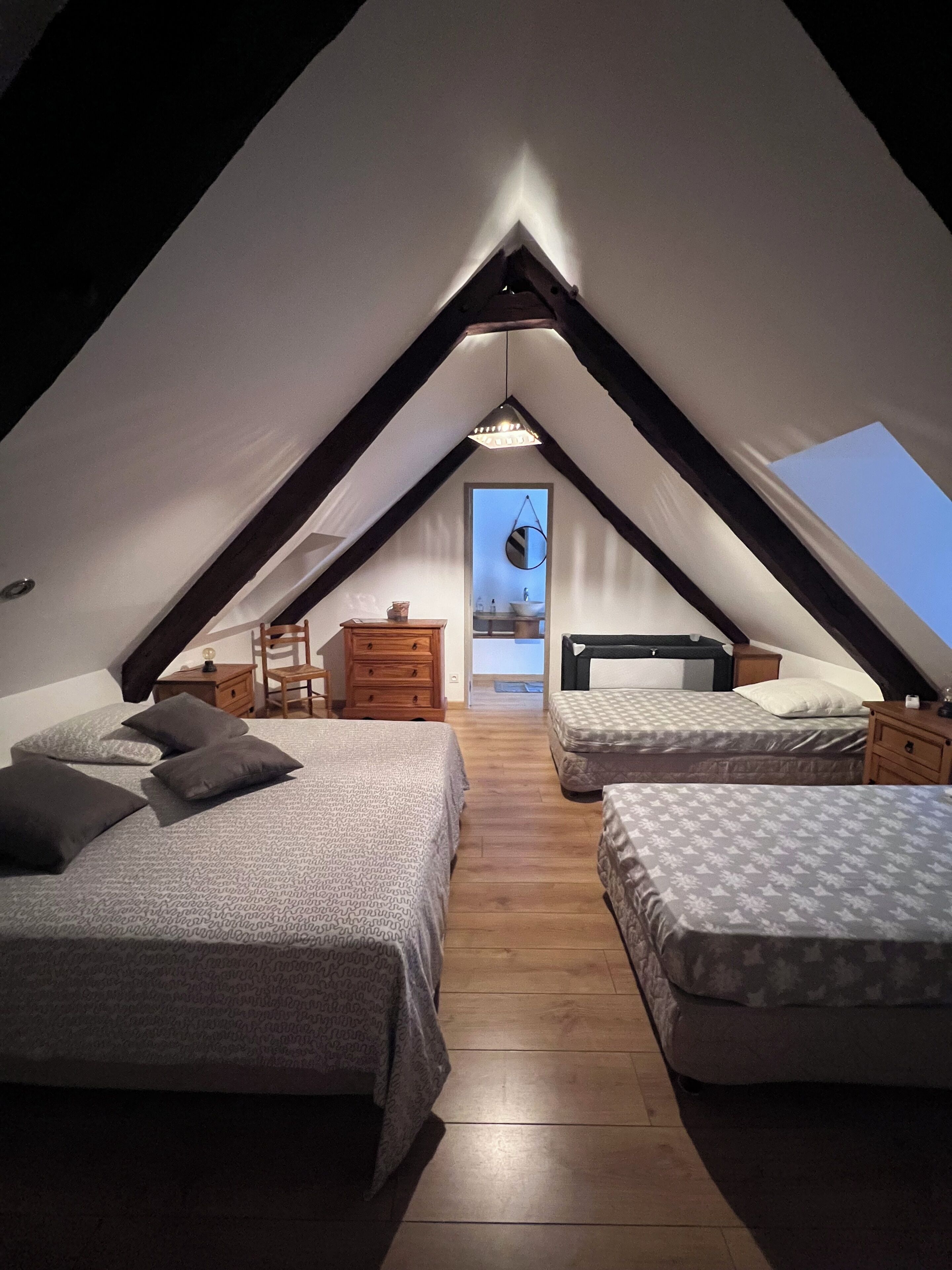 Een zolderkamer met een puntdak, twee bedden, een houten dressoir, een klein tafeltje en een spiegel.