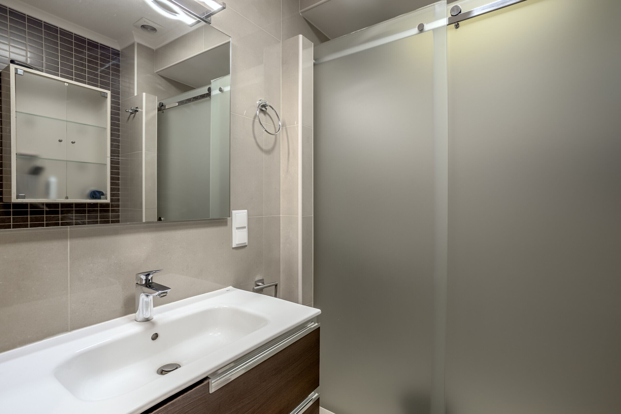A modern bathroom with a white sink, a mirror, and a glass-enclosed shower.