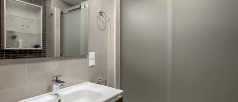 A modern bathroom with a white sink, a mirror, and a glass-enclosed shower.