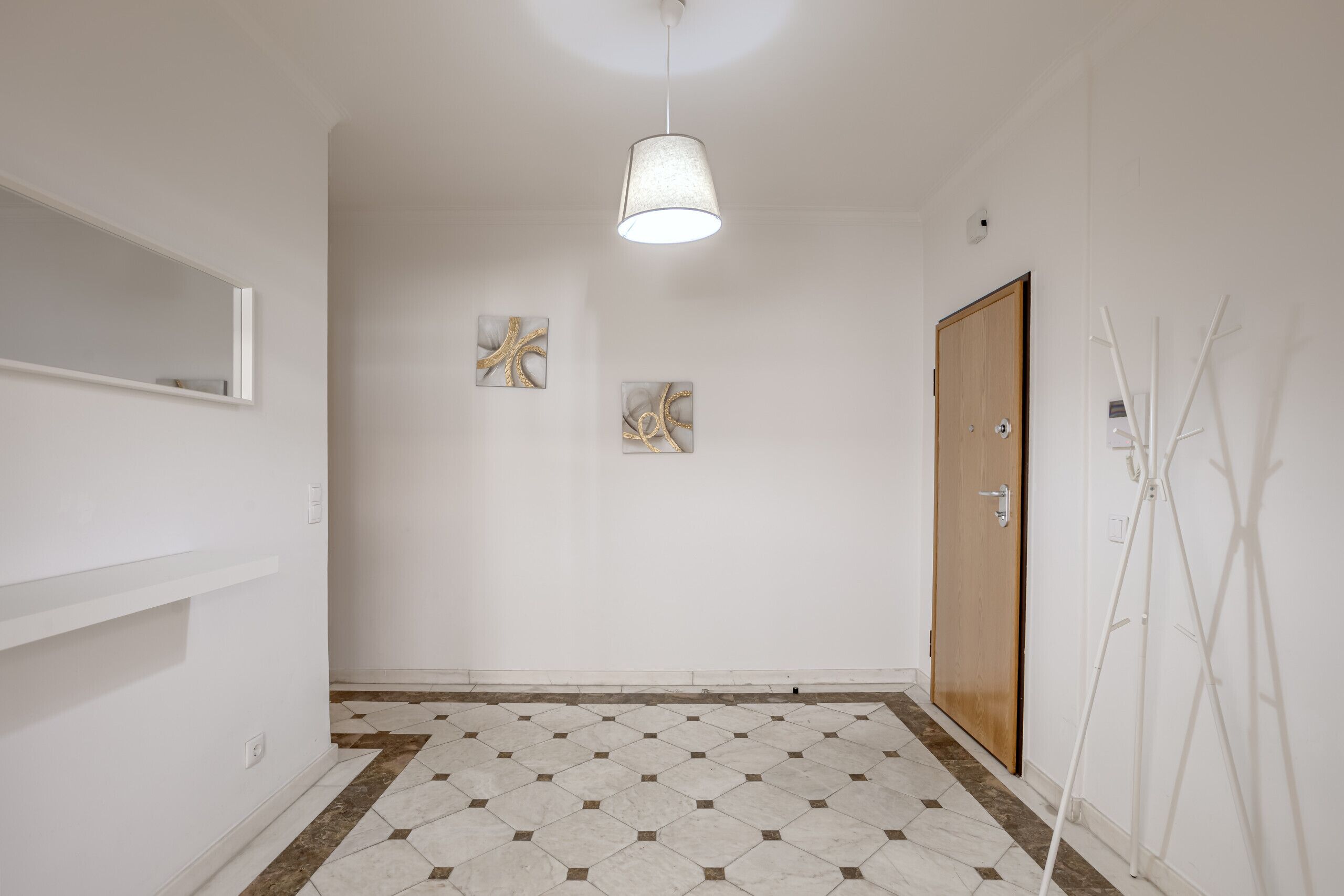 Un couloir doté d’un sol carrelé, d’un luminaire suspendu, d’une porte en bois et de deux œuvres d’art accrochées au mur.