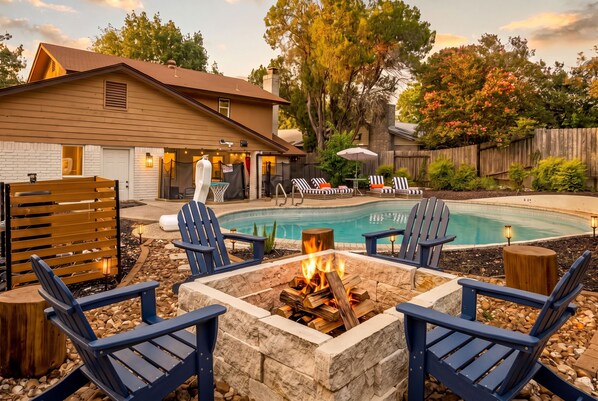 A backyard with a swimming pool, lounge chairs, a fire pit, and a wooden deck.