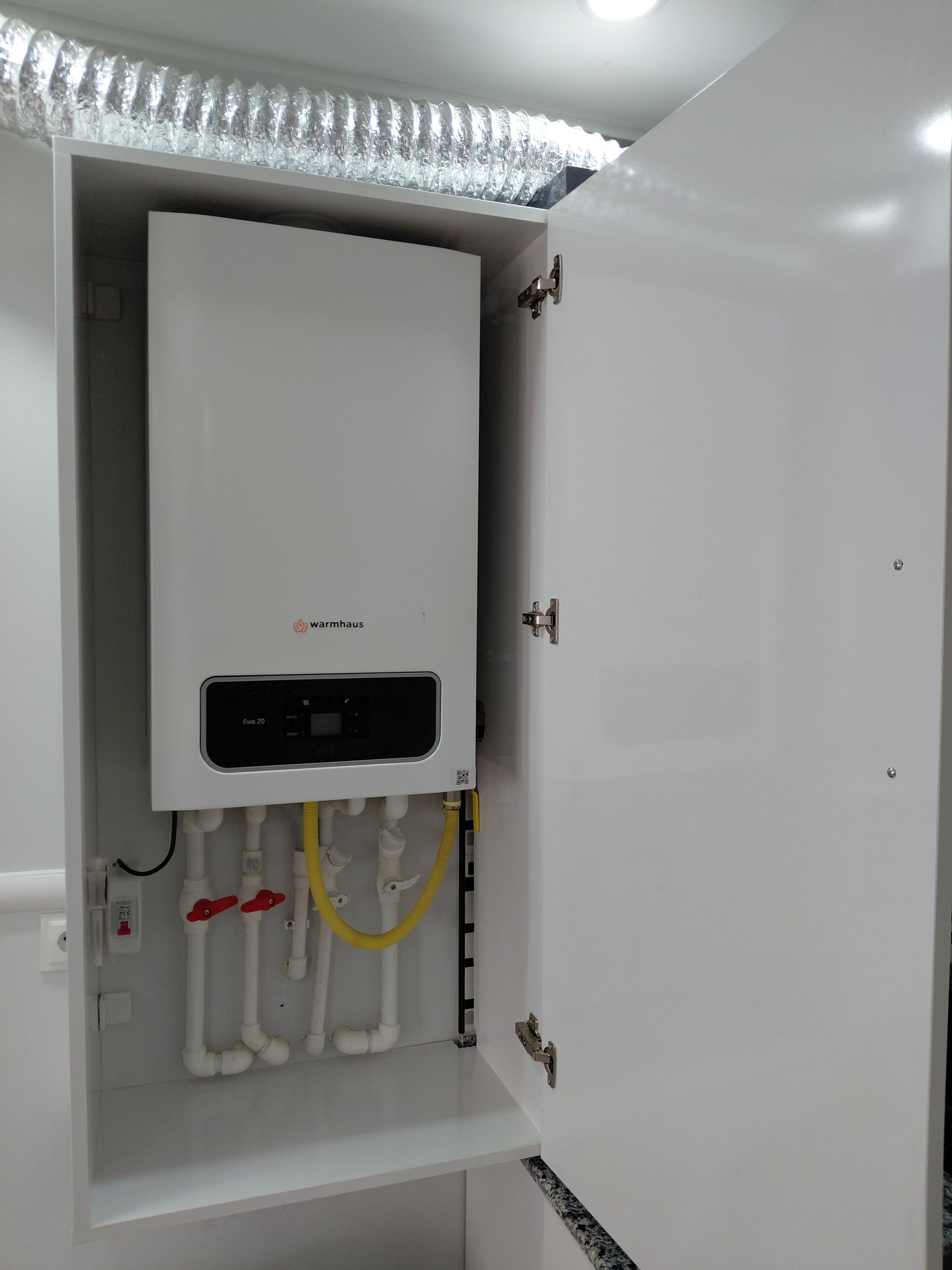 A white water heater with a control panel, connected to white pipes and a yellow hose.