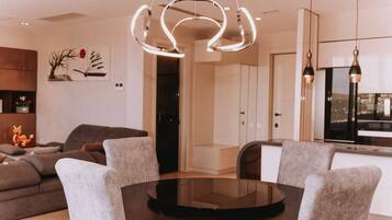 A modern living room with a round glass table, grey upholstered chairs, a contemporary light fixture, and a minimalist decor.