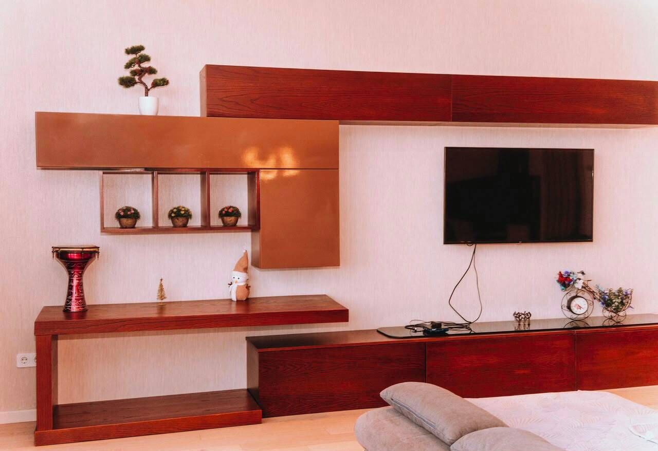 A modern living room with a flat-screen TV mounted on the wall, a wooden console table with decorative items, and a sofa.