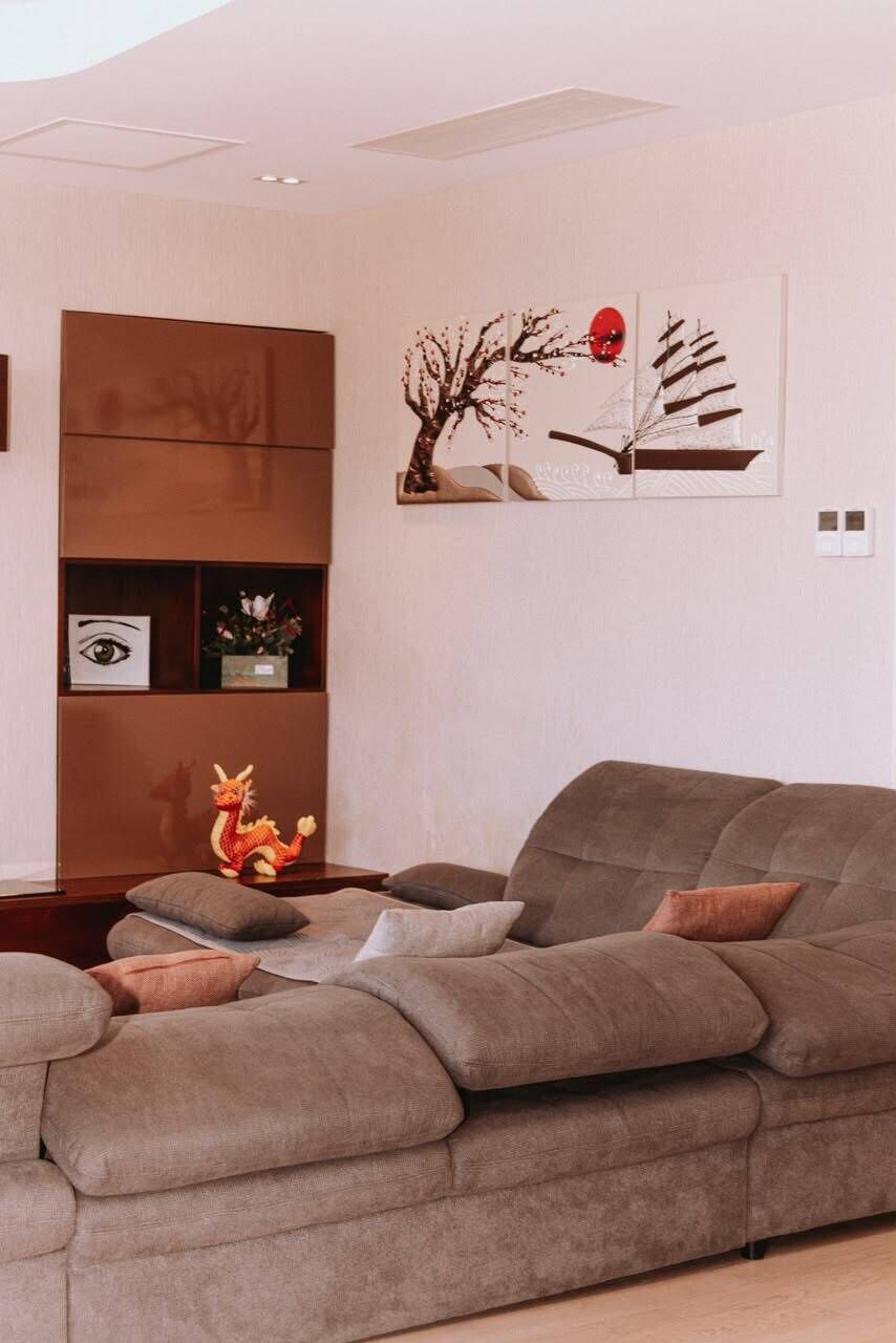 Un salon moderne avec un canapé d’angle, une sculpture d’arbre décorative et une étagère contenant divers objets, dont une figurine de dragon.