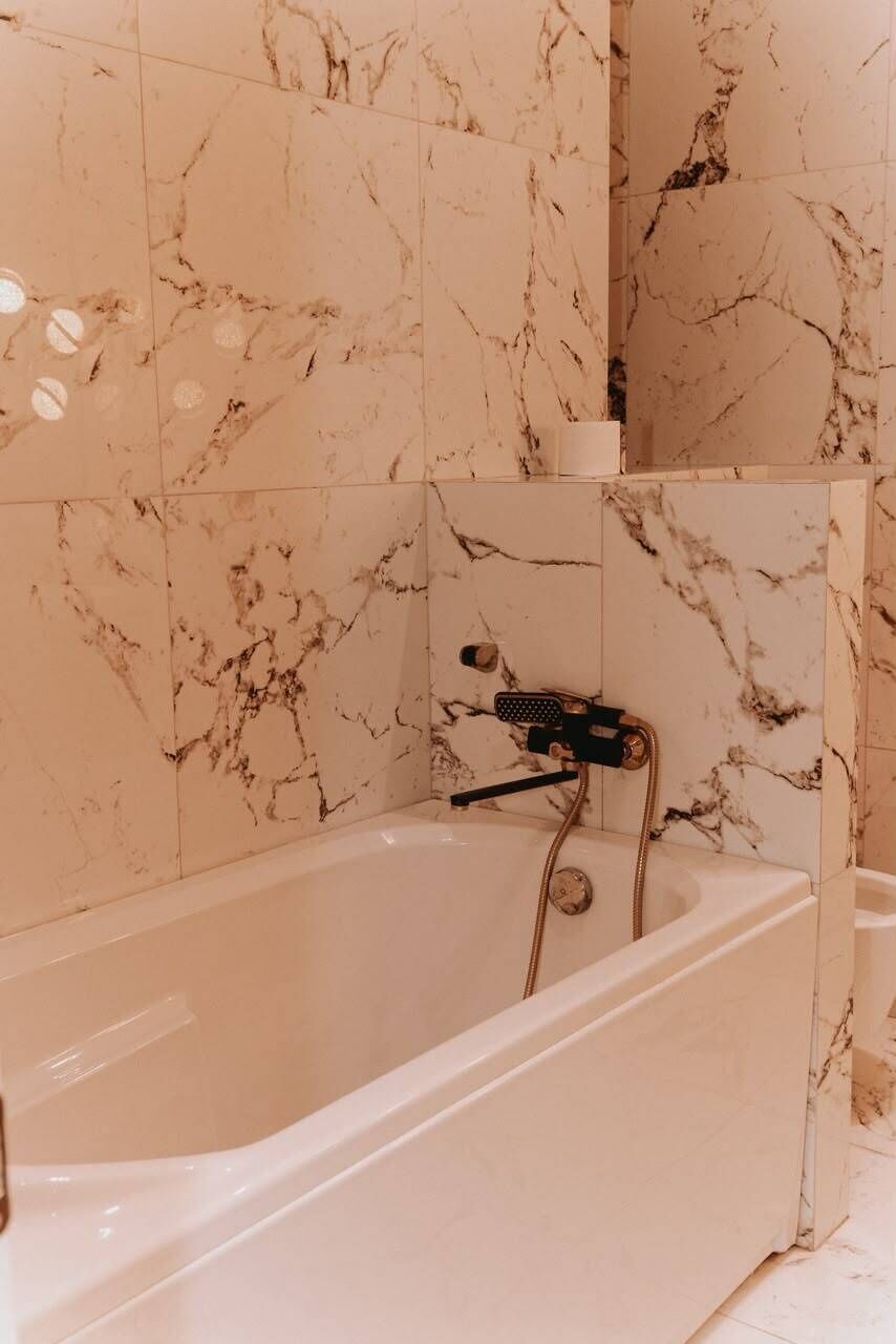 Une salle de bain avec une baignoire, des murs en marbre et un espace douche.