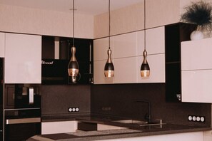 Una cocina moderna con lámparas colgantes, horno empotrado y pileta.