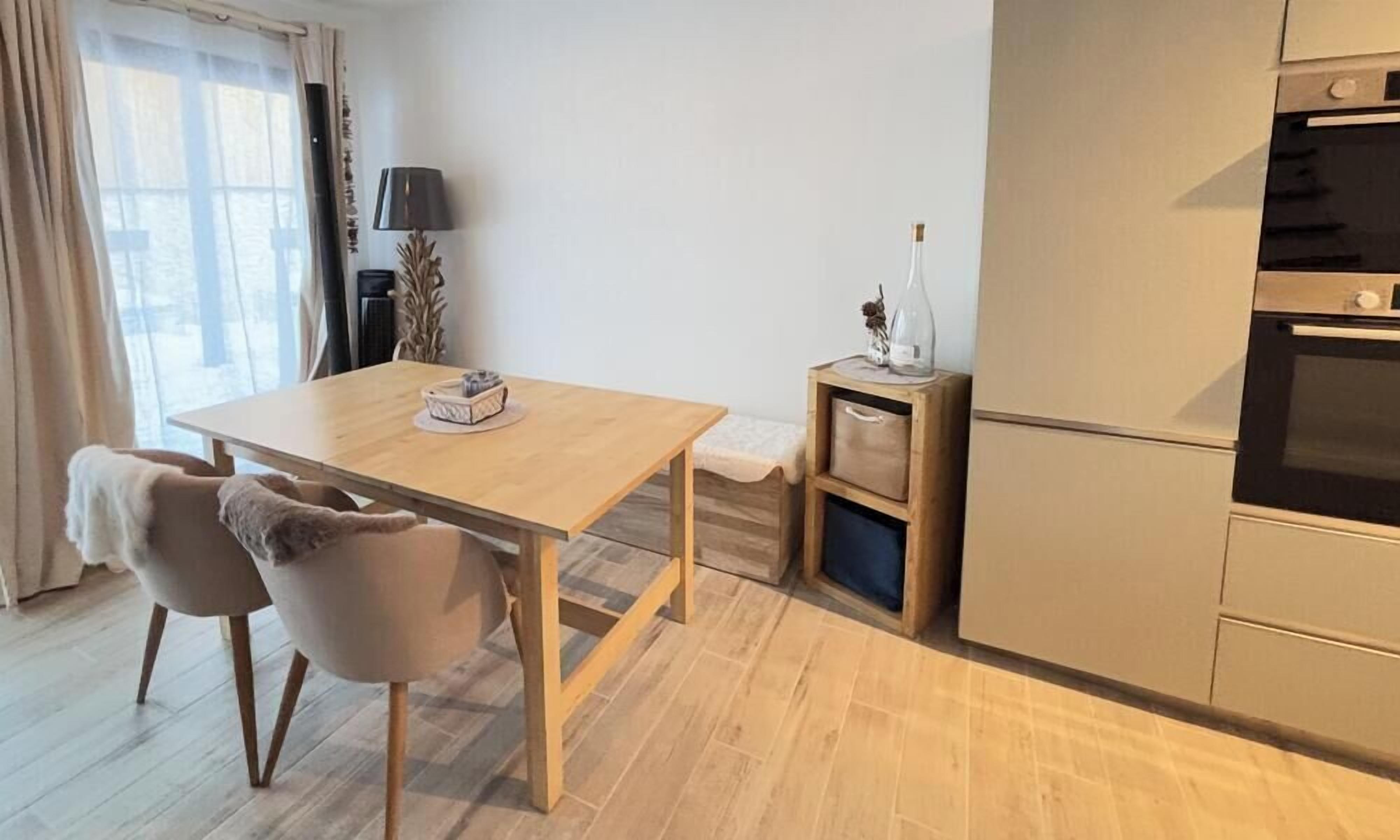 Una cocina moderna con una mesa de madera y sillas, una mesita auxiliar con una botella y un horno empotrado.