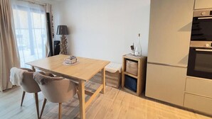 Een moderne keuken met een houten tafel en stoelen, een klein bijzettafeltje met een fles, en een inbouwoven.