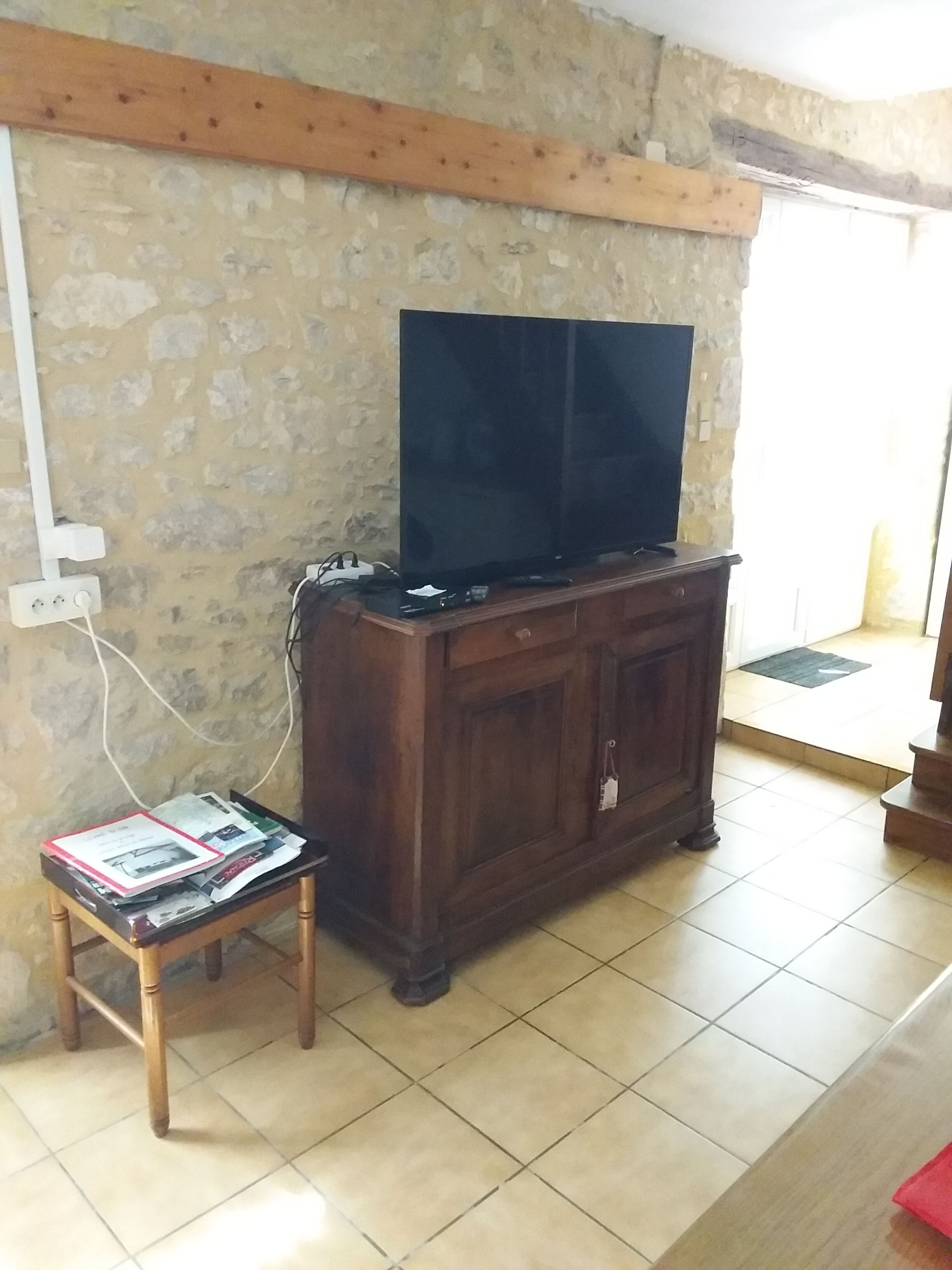 Ein Zimmer mit Fernseher auf einer Holzkabine, einem kleinen Tisch mit Zeitschriften und einer Steinwand.