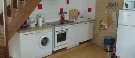 Cocina compacta con lavadora, horno y una mesa de comedor con una botella.