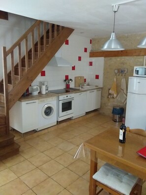 A compact kitchen with a washing machine, oven, and a dining table with a bottle. - La Grange Vacation Rental in the Périgord Noir (Allas-les-Mines)