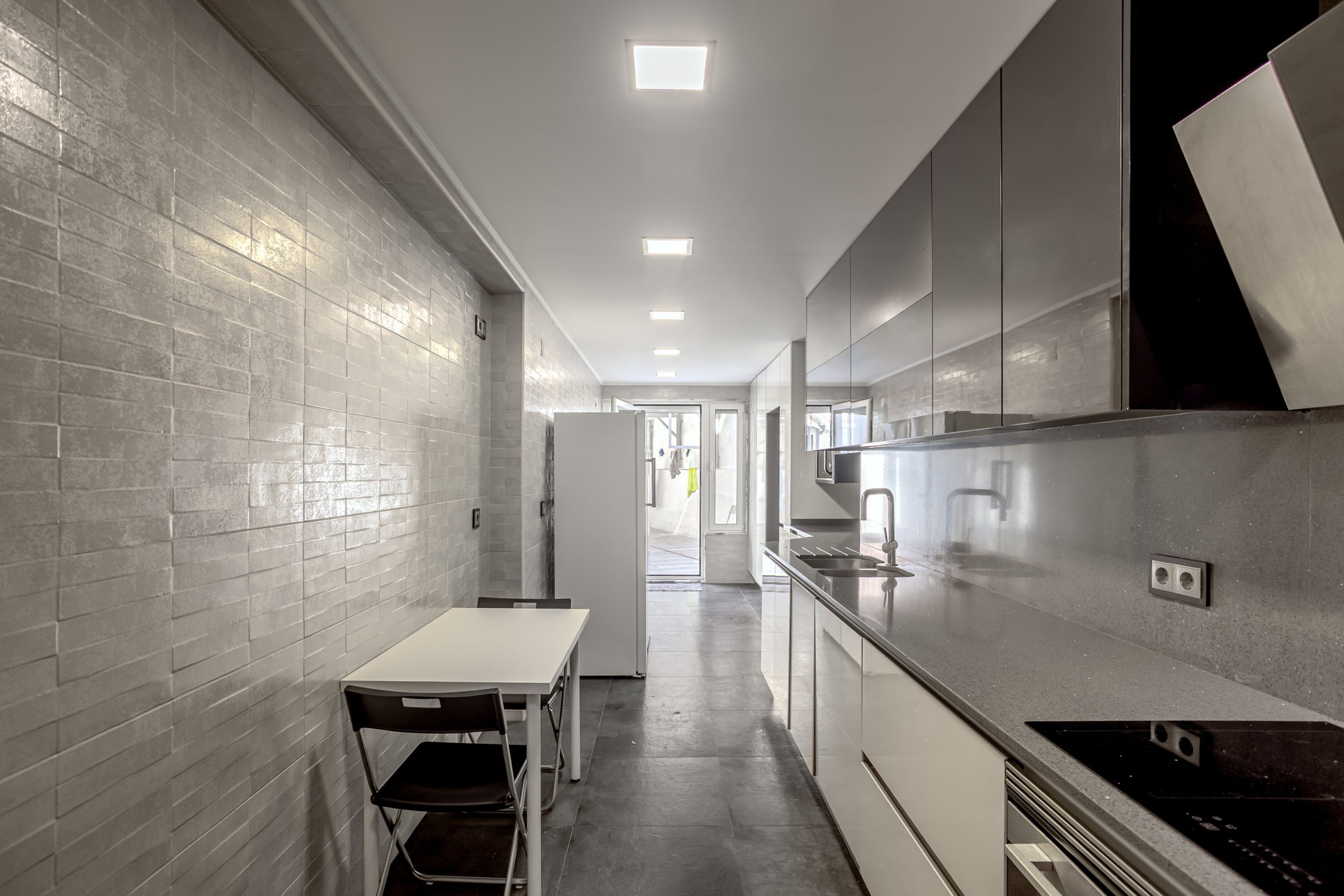 A narrow kitchen with a white table and chairs, a refrigerator, and a stove.