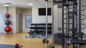 Ein Fitnessraum mit Trainingsgeräten, Kurzhanteln und einem an der Wand montierten Fernseher.
