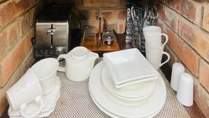 Una cocina compacta con microondas, estantes con vajilla y una pequeña mesa con tazas y platos.