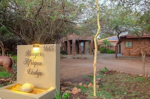 A sign for Kruger Afrique Lodge with a number 1615, a water feature, and a brick building with a tiled roof.