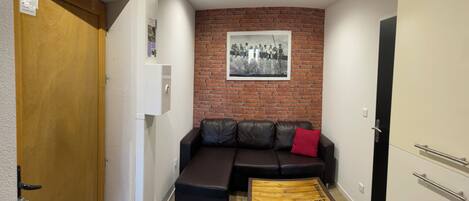 A room with a brick wall, a black leather sofa, a wooden coffee table, and a door with a sign.
