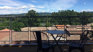Un balcon avec deux chaises et une petite table, donnant sur un quartier résidentiel avec des maisons et des arbres.