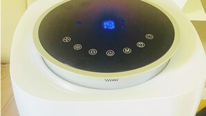 Un purificateur d’air blanc doté d’un panneau de commande circulaire et d’une grille d’aération située en bas.