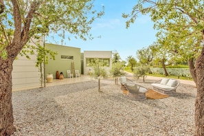 A modern outdoor patio with wicker furniture, a stone wall, and a building with large windows. - Fior di Noto, Golden Luxe Sicily (Noto)