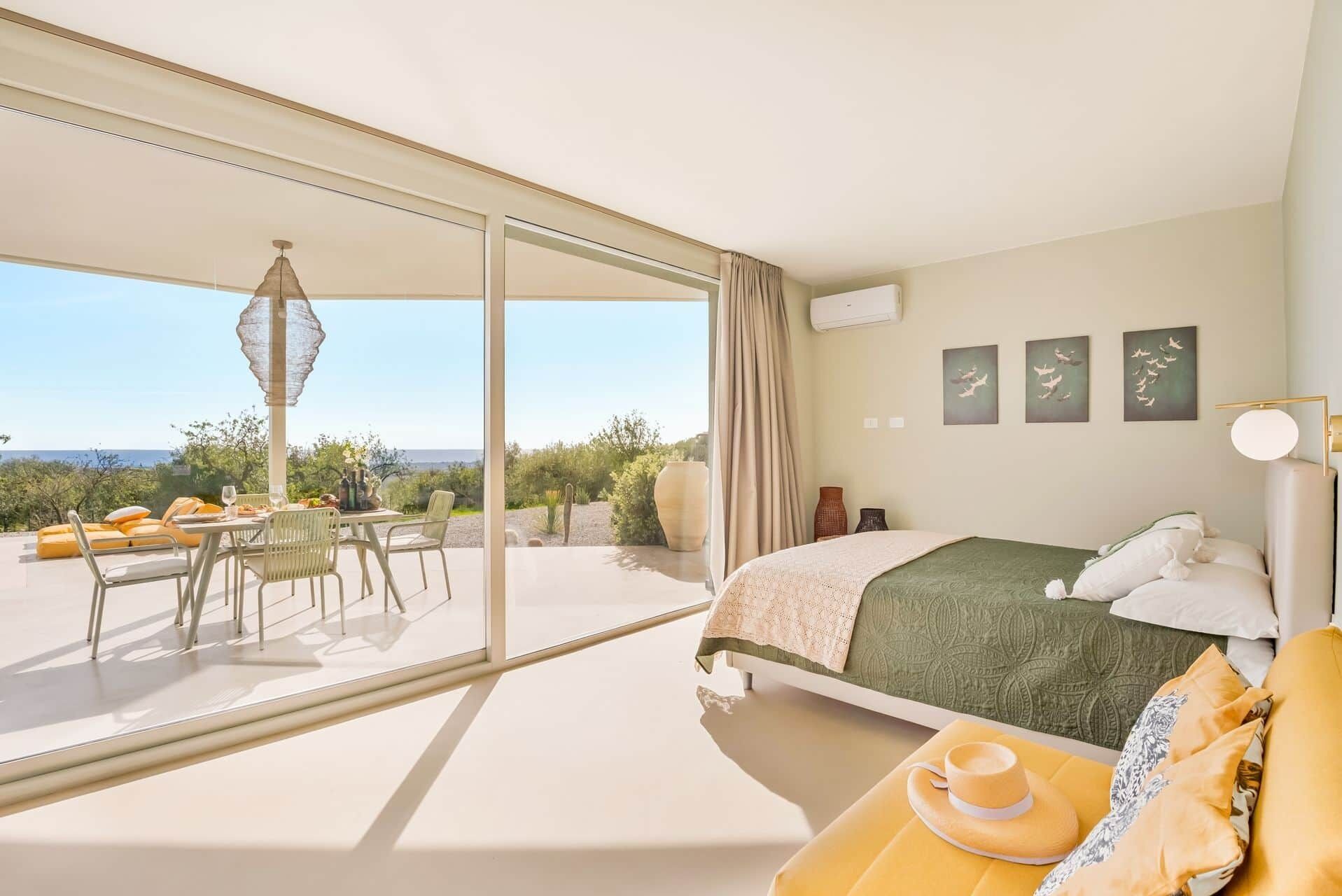 Une chambre avec un lit, un coin repas avec une table et des chaises, et une vue dégagée grâce à de grandes fenêtres.