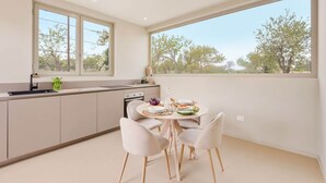 Cocina moderna con comedor, ventanas amplias y vista a árboles.