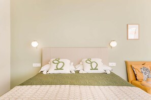 A bed with a green bedspread, two white pillows with green designs, a beige headboard, and two wall-mounted lights. - Fior di Noto, Golden Luxe Sicily (Noto)