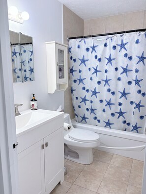 A bathroom with a white sink, a toilet, a cabinet, and a shower curtain with a starfish pattern. - Cozy 2-bedroom apartment 22 minutes from Montreal (La Prairie)